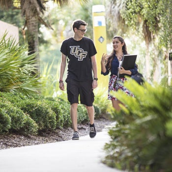 male and female ucf students walking around campus, surrounded by trees and plant life