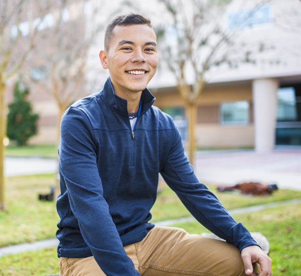 male ucf student wearing long sleeve blue shirt with khaki pants sitting outside and smiling at camera