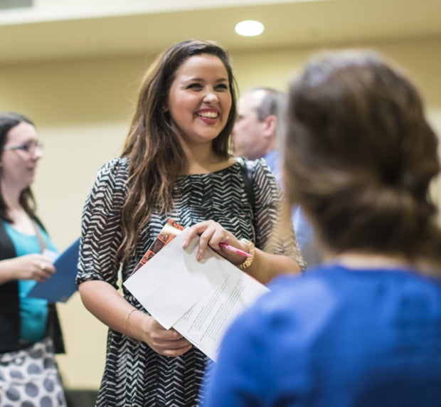 ucf student smiling and holding papers with other people faded in background and foreground