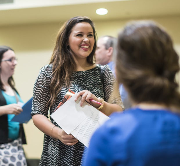 female ucf smiling and holding papers with other people faded in background and foreground