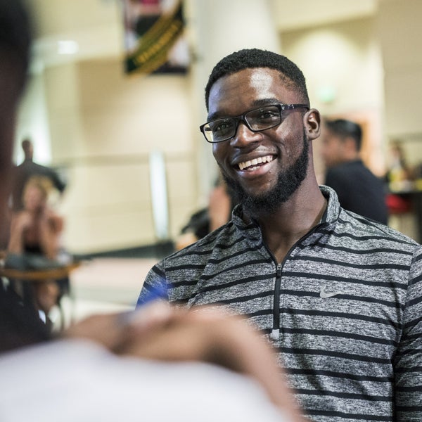 male ucf student in glasses and a black and grey striped polo, smiling at someone to the left of camera