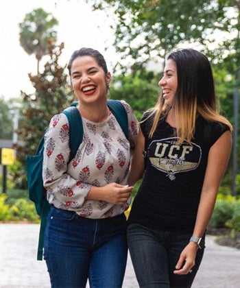 two ucf students with dark hair, walking outside while laughing