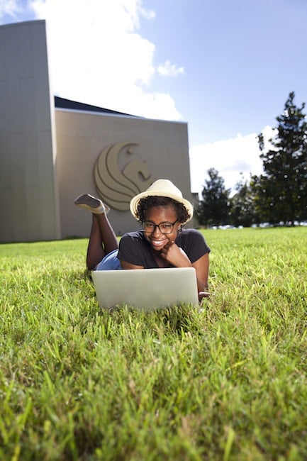 Student using computer in grass outside Welcome Center