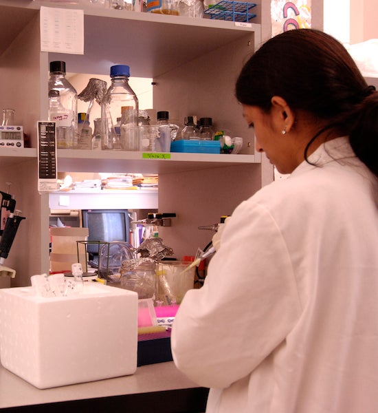 female student in white lab coat working in a lab