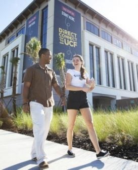 2 ucf students walk by direct connect to ucf sign on campus building