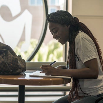 ucf student filling out admissions forms at a table in front of glass etched pegasus logo