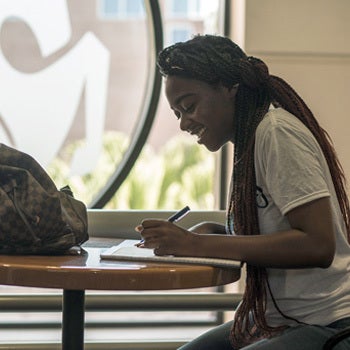 female ucf student filling out admissions forms at a table in front of glass etched pegasus logo