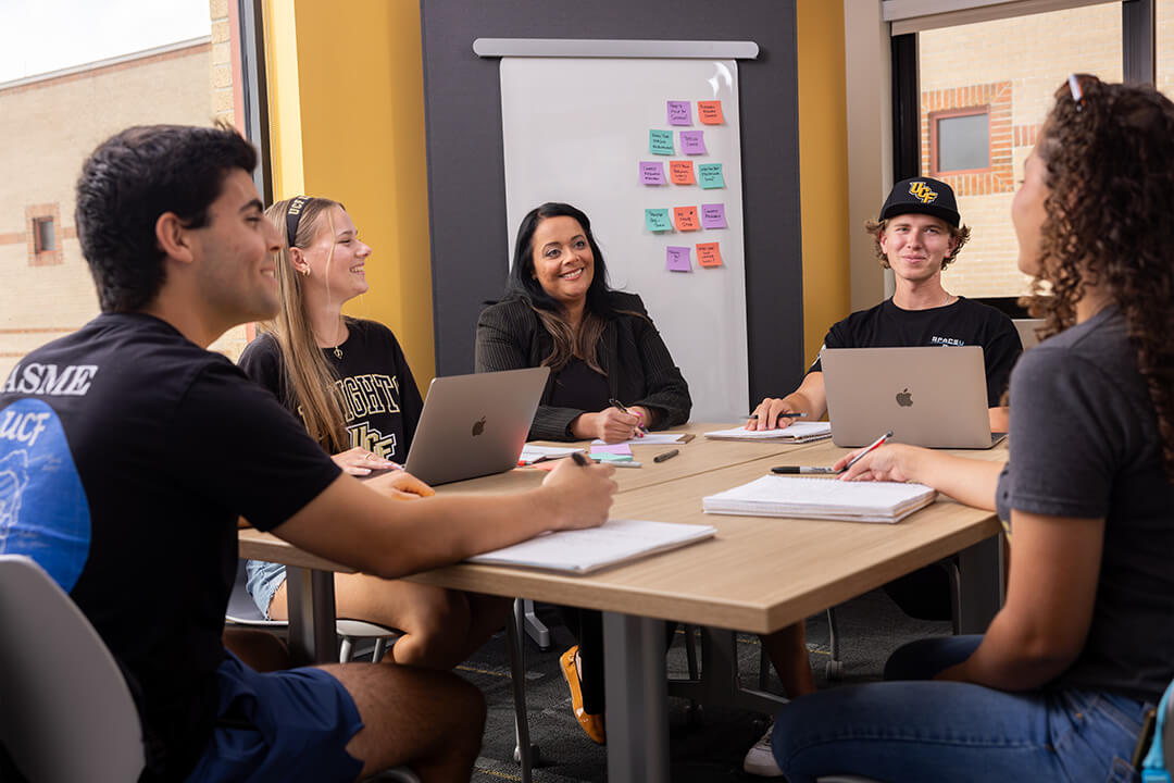 UCF students collaborating around a table with laptops and notes.