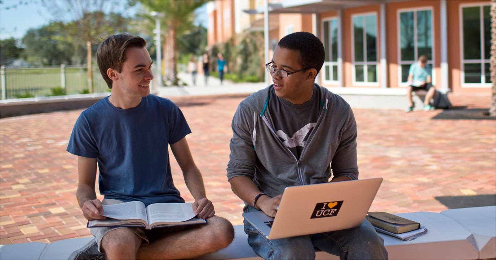two ucf students sitting outside on a bench studying together