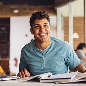 Student smiles in front of textbooks.