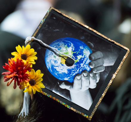 Graduation cap with the image of the earth being held by two hands and a flower growing out of the center