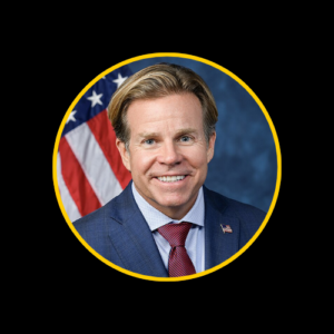 U.S. Representative Mike Haridopolos, a Caucasian man with short, neatly styled hair, wearing a dark suit, white shirt, and a patterned tie, smiling confidently in a formal portrait with an American flag in the background. 