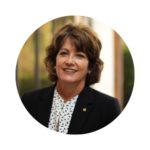 Janet Owen, Vice President for Government and Community Relations at UCF, smiling outdoors in a professional portrait. She is wearing a black blazer over a white patterned blouse, with a UCF pin on her lapel.