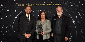 President Cartwright and Provost Johnson pose with a faculty member holding an award 