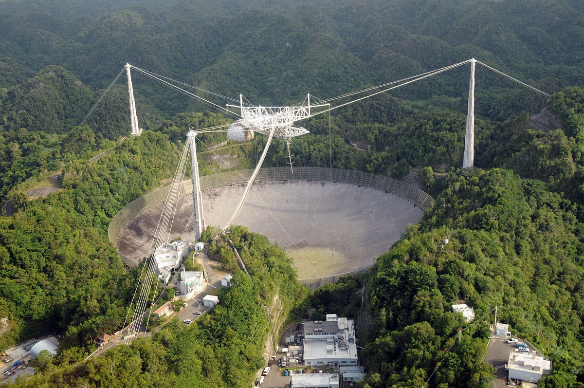 A giant concrete crater is surrounded by green, luscious trees.