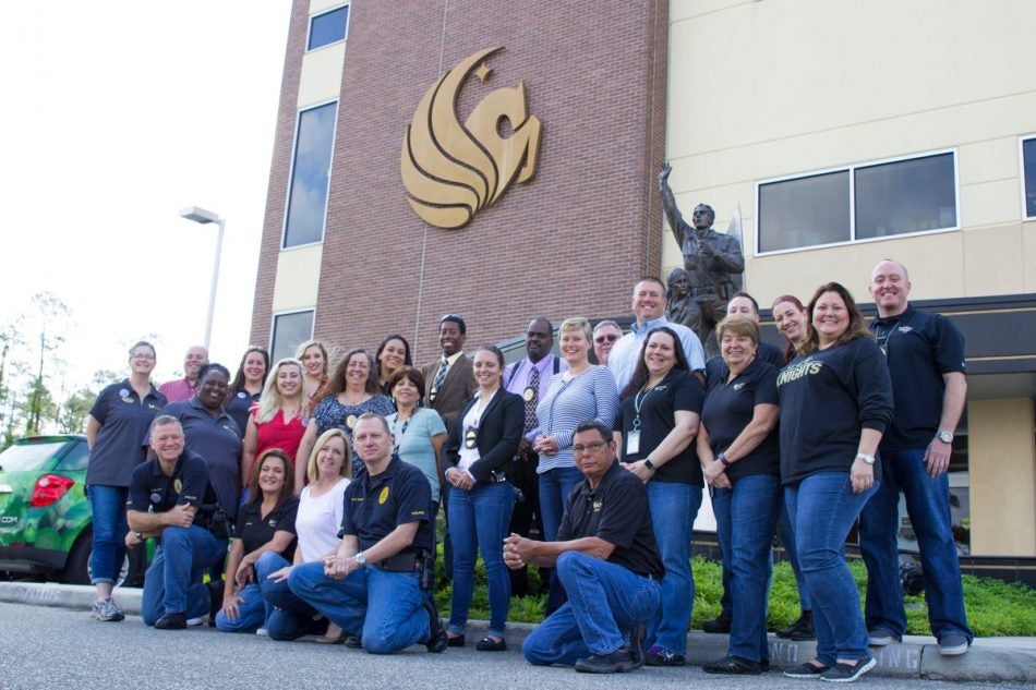 ucf police department staff and officers in front of police building with gold pegasus logo on brick wall