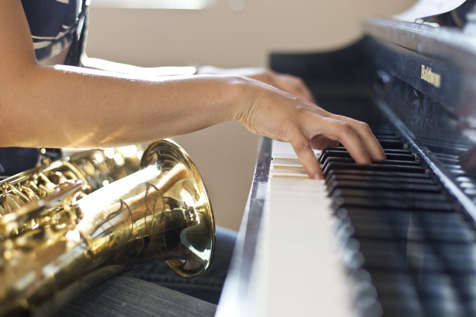 woman sitting, playing a piano with a saxaphone in her lap