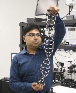 man with blue collared shirt, black hair, and glasses holding up a dna model