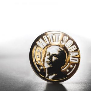 Image of gold pin that says Hitt Squad in white with a monochrome image of John Hitt.
