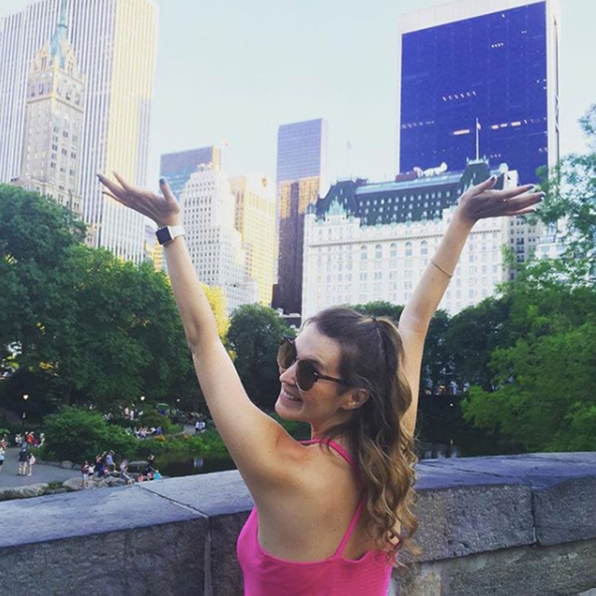  Woman in pink shirt with her back to camera smiles over her shoulder with New York City skyscrapers in the background