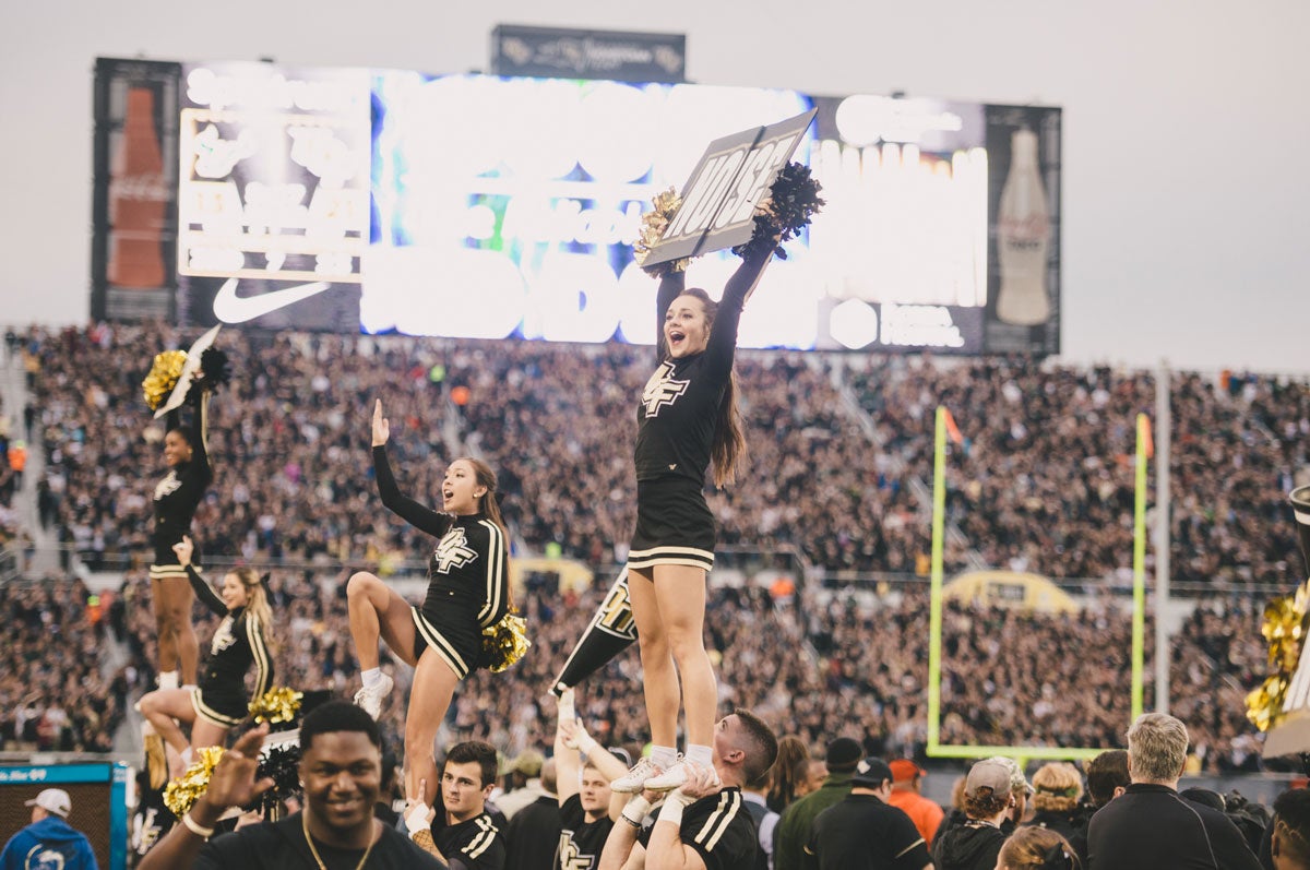 Cheerleaders dressed in black hold up "get loud" signs in front of UCF crowd at Spectrum Stadium