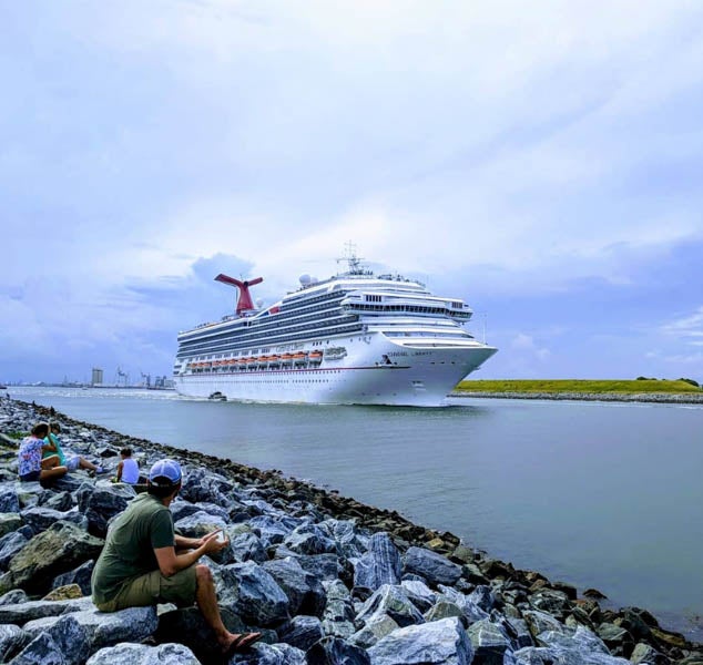 people sitting on rocks watching a cruise ship pass by at Jetty Park at Cape Canaveral