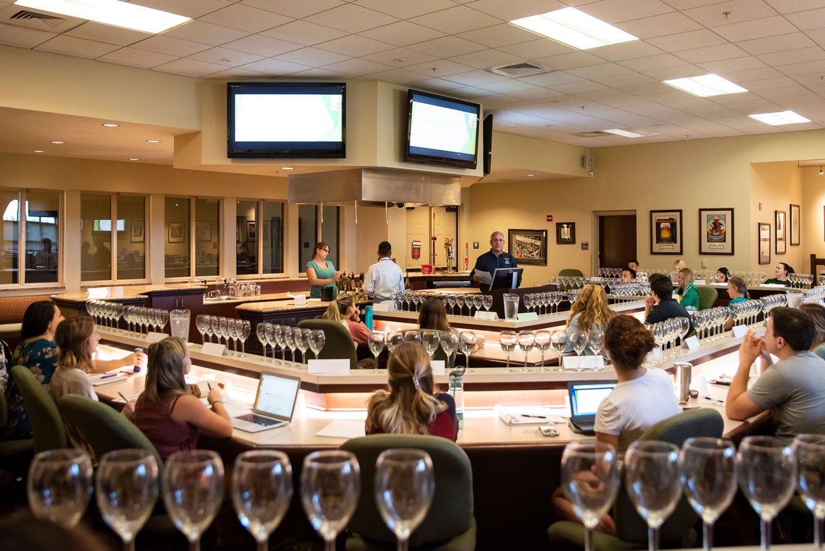 Wide view of a classroom with tiered rows and students with their laptops sitting in their seats