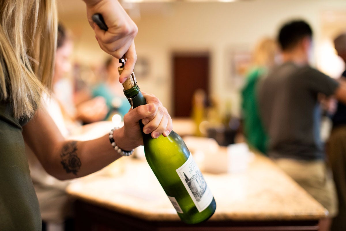 closeup of two hands hold a green wine bottle and attempting to remove the cork