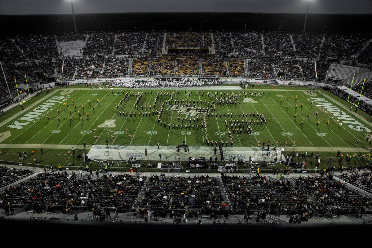 wide shot of a football stadium at night with UCF logo spelled out by the band on the green field
