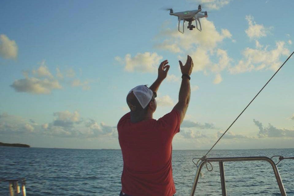 Man in a red shirt and baseball hat releases flying drone from boat