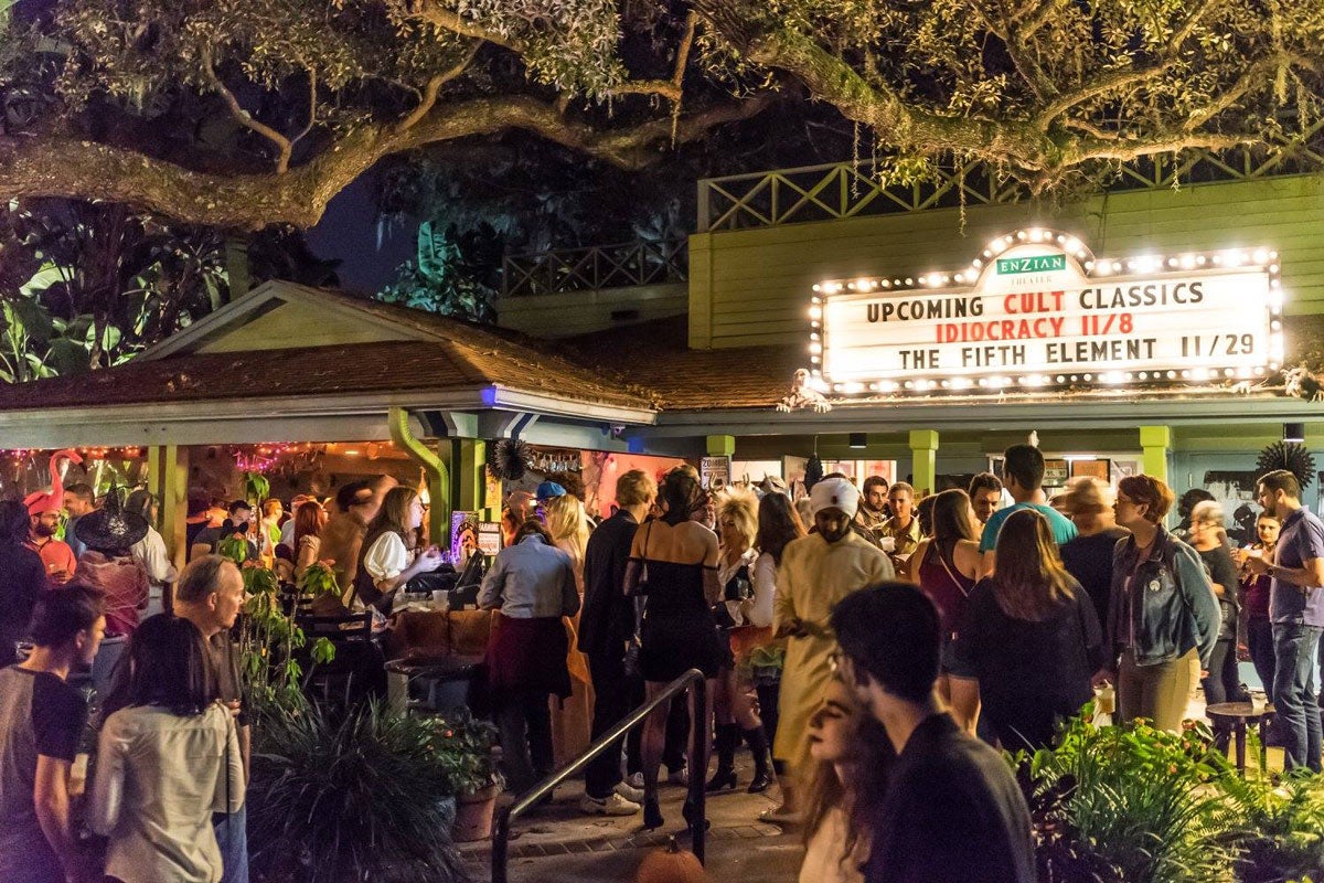 Green theater building with a marquee in lights, an oak tree hovering over it and many people standing outside