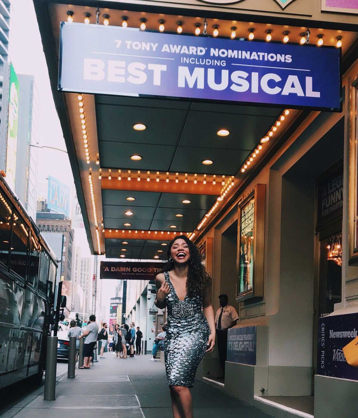 Woman in gray dress stands under theatre marquee