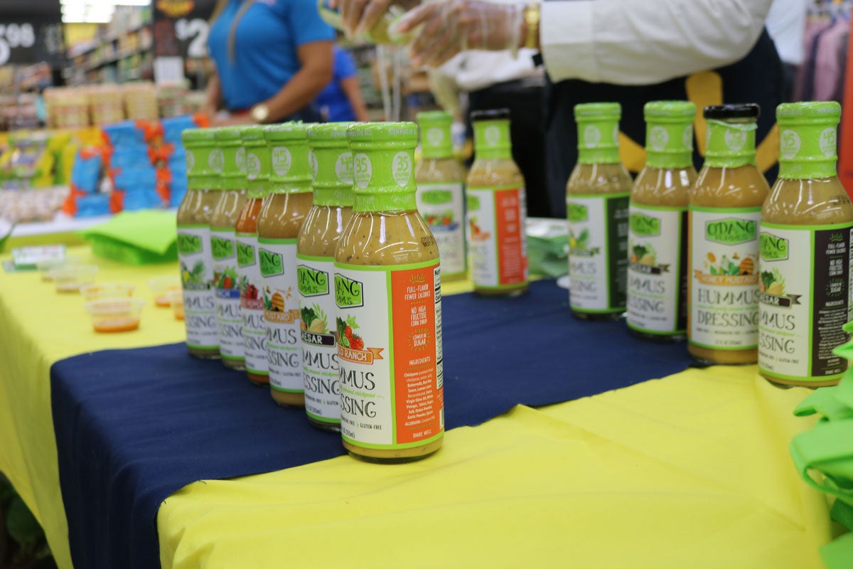 rows of salad dressing bottles with green tops on a table with a blue and yellow table cloth
