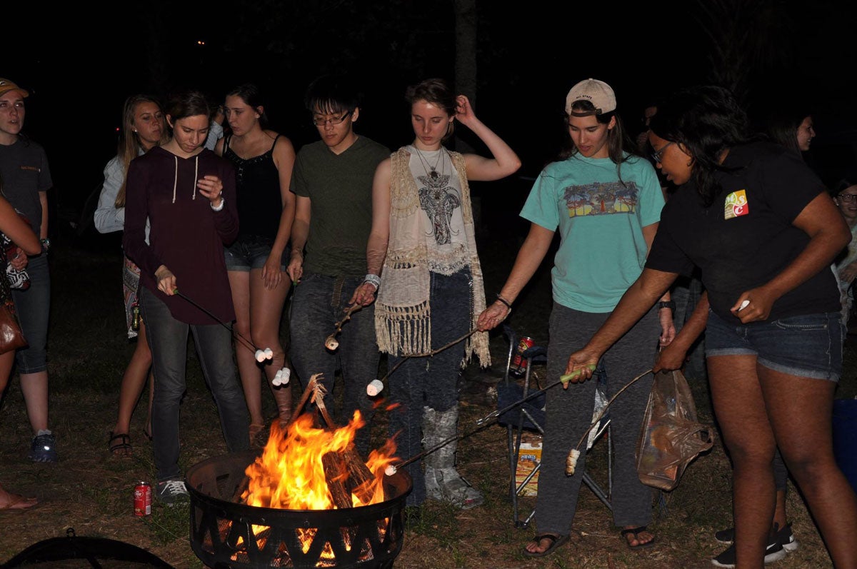 Group of students roasting marshmallows at night over a campfire