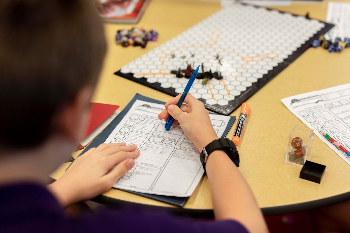 over the shoulder view of a teenager filling out a sheet for a board game he is playing on a circular table