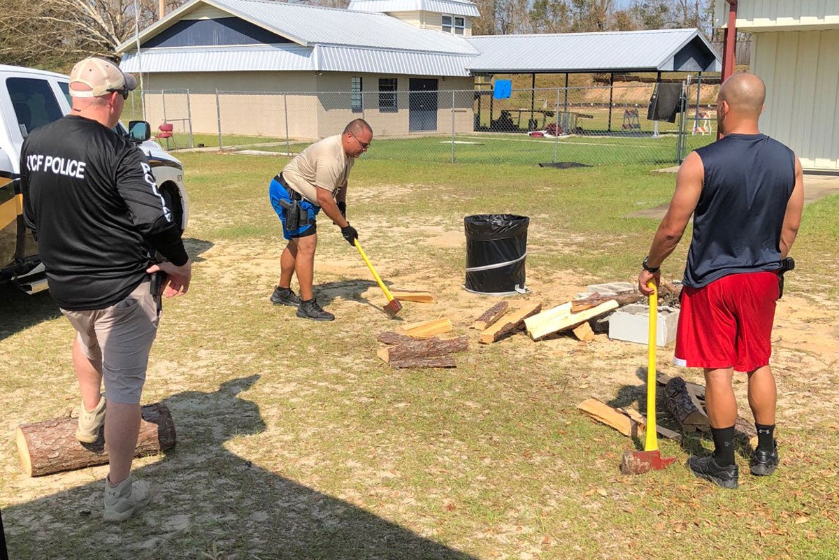 A man in a field chops wood while two other men observe behind him