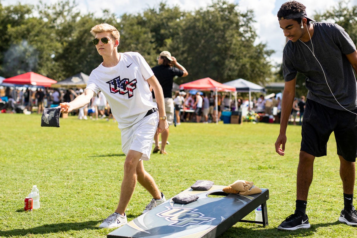 Two men play cornhole on grass