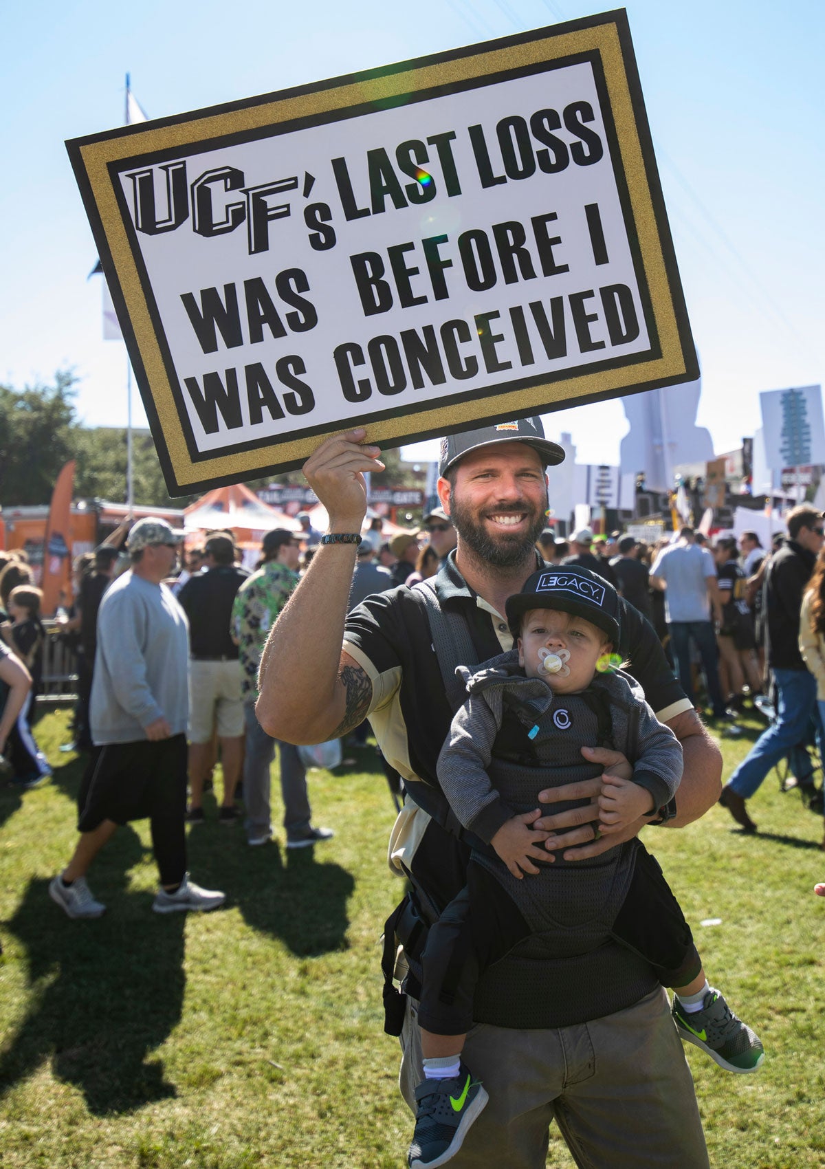Man holding a baby with a sign that read "UCF's last loss was before I was conceived"