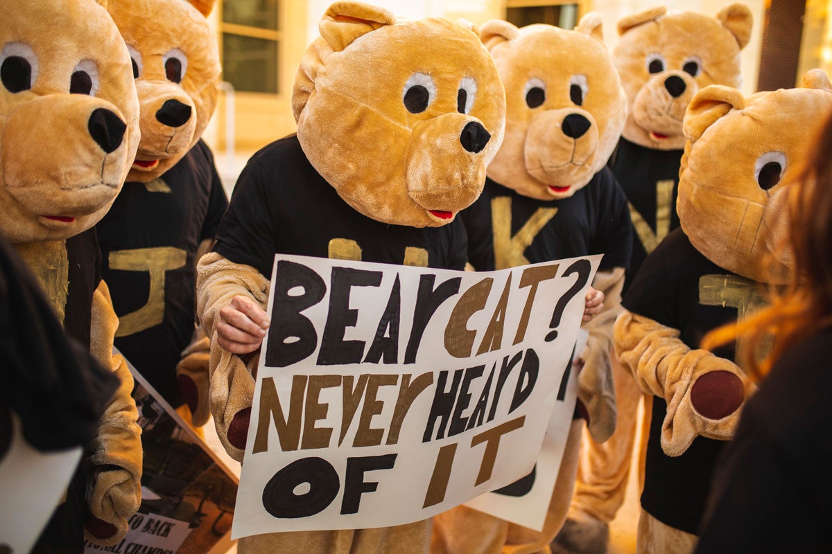 People dressed like golden color bears hold a sign that says Bearcat? Never heard of it.