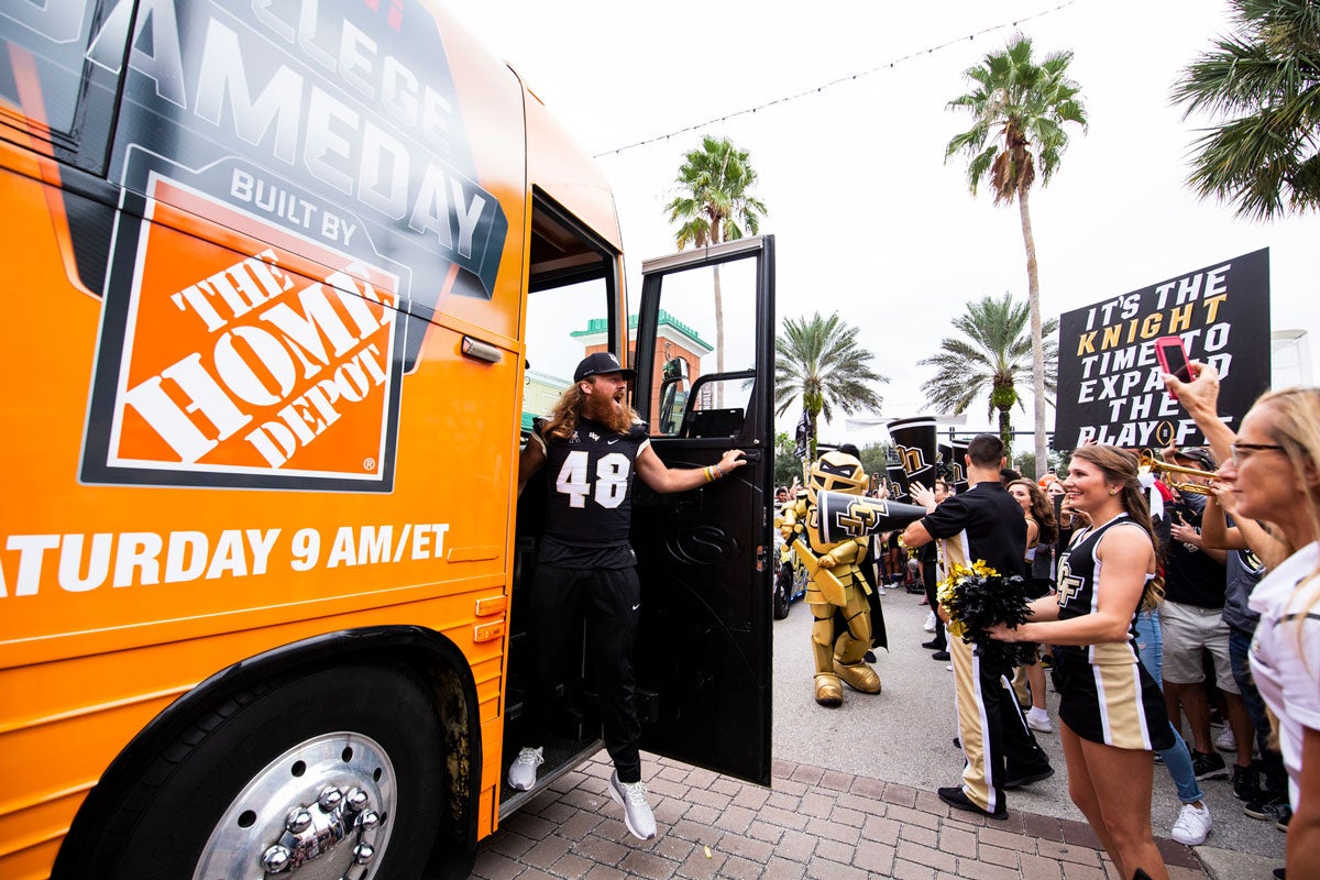 UCF Football player Mac Loudermilk wearing his #48 jersey steps off Orange bus with Home Depot logo and greets cheering fans 