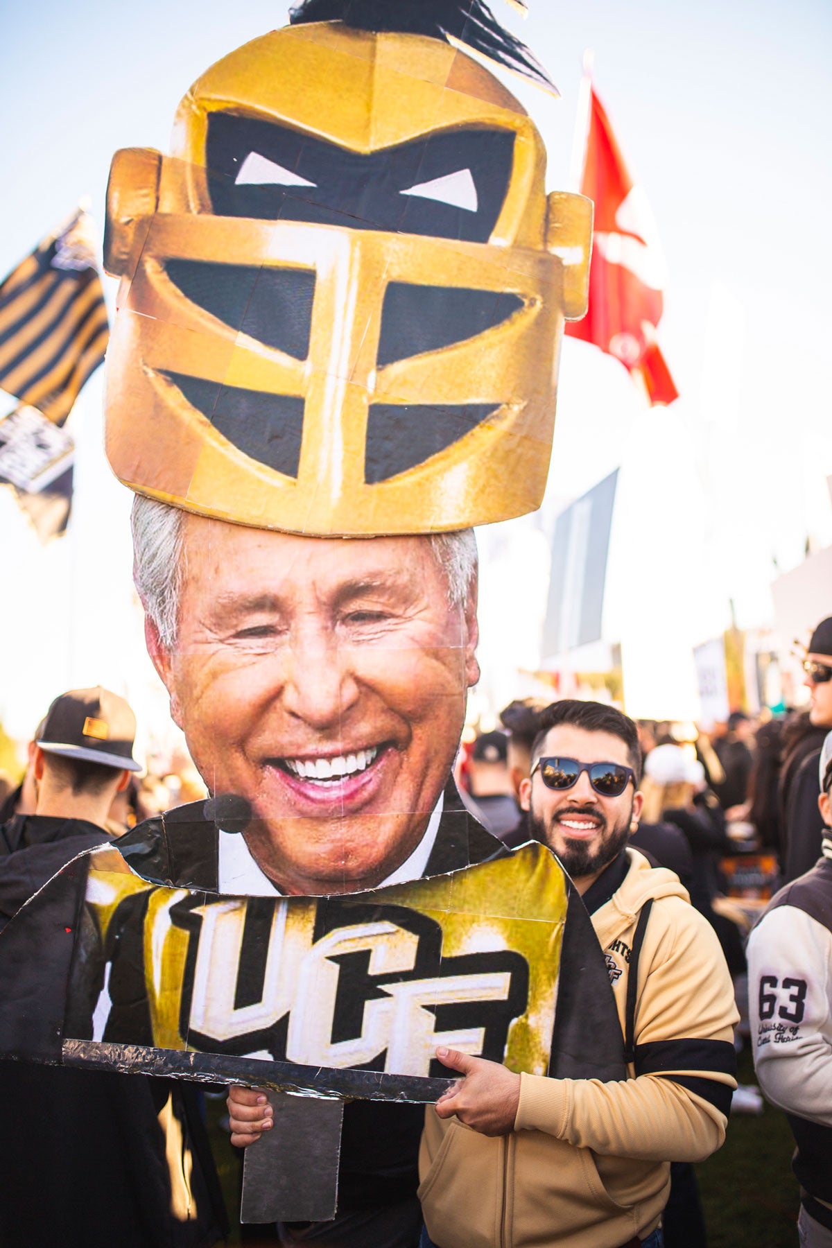 Man wearing a black and gold jersey holds a cutout of Lee Corso head with Knightro mask