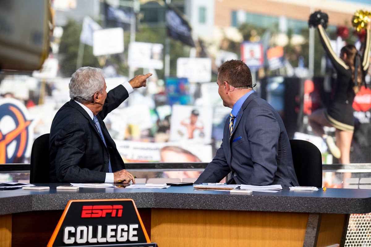 ESPN analysts Lee Corso and Kirk Herbstreit look back at the crowd from their desk chairs
