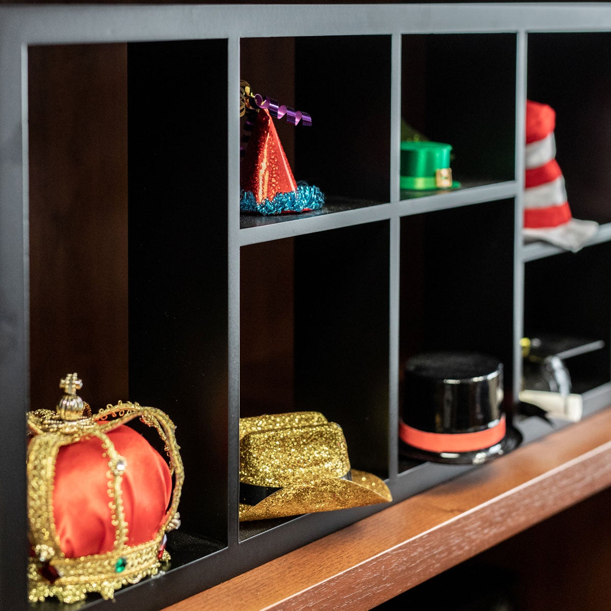 a black horizontal cube shelf with hats of different styles featuring a royal crown, cowboy hat and top hat