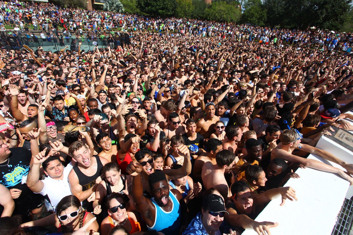 thousands of college students crammed into a pond with their hands raised on a sunny day