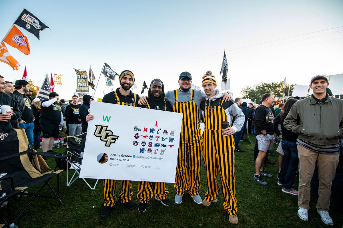 Four men wearing black and gold stripped overalls hold a sign