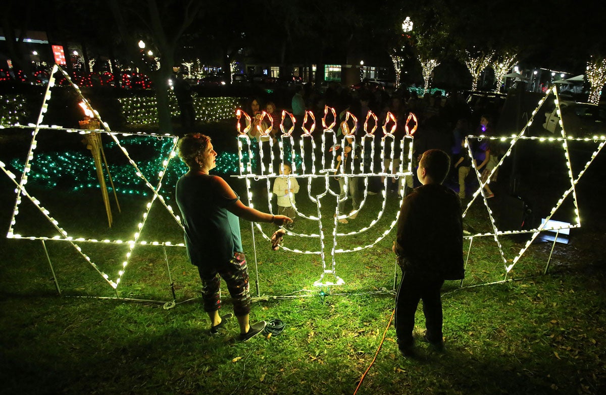 Two people look at lights shaped like a Menorah and Star of David on a grassy lot