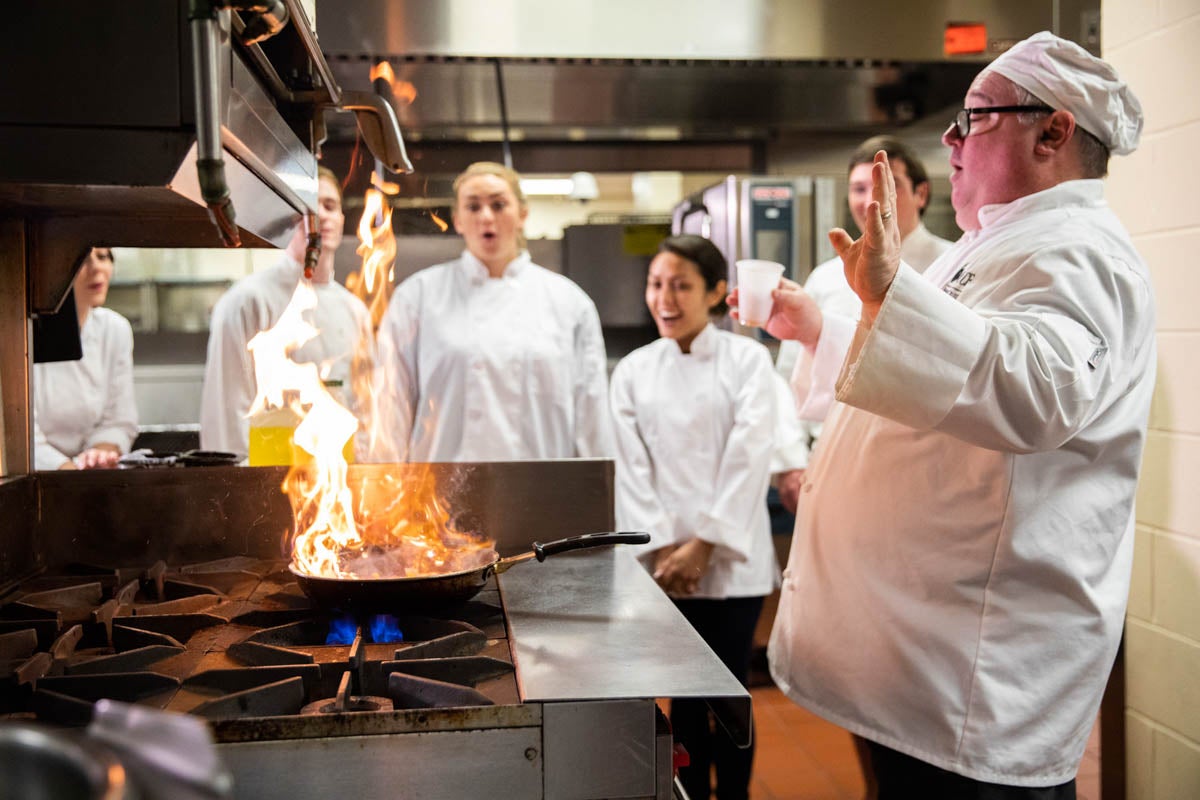 An instructor at the Rosen College of Hospitality Management demonstrates how to put out a fire during a cooking class.
