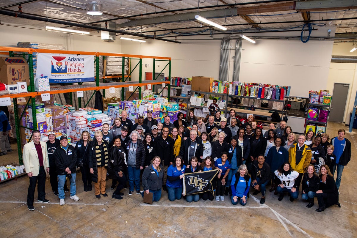 A large group of dozens of people wearing UCF black and gold pose for a photo in Arizona Helping Hands storehouse