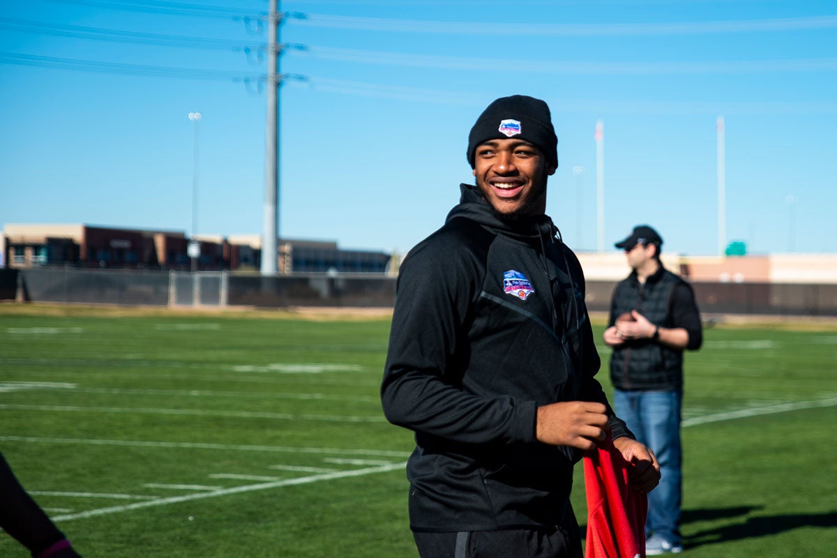 Darriel Mack Jr wears a longsleeve black shirt and beanie and smiles over his shoulder on football field