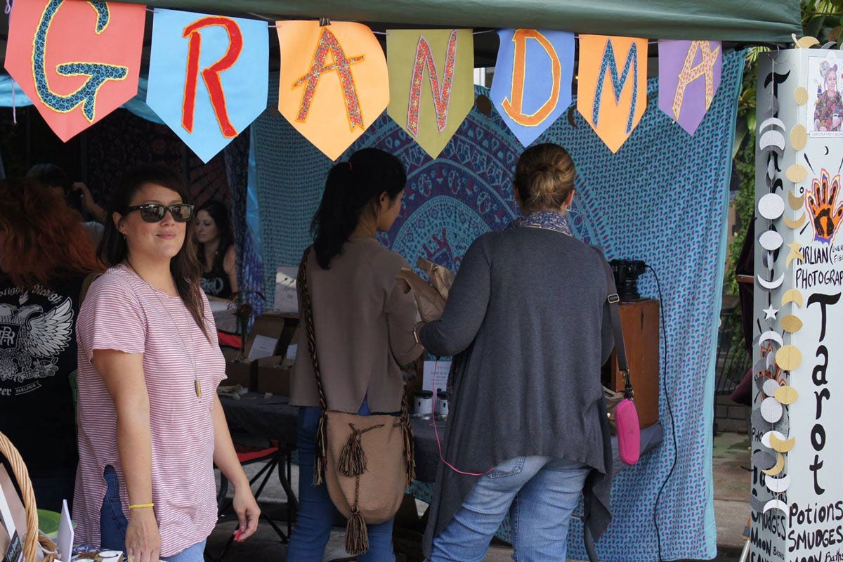 Three people shopping under a tailgate tent with a multi-colored banner hanging from the roof that reads Grandma